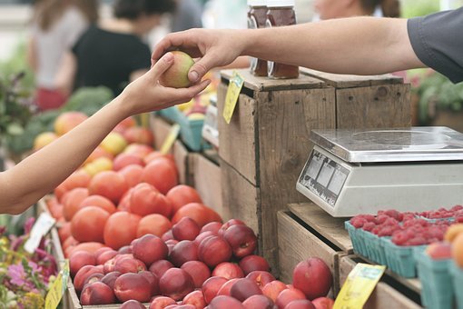 A woman handing an apple to a man at a farmers' market.