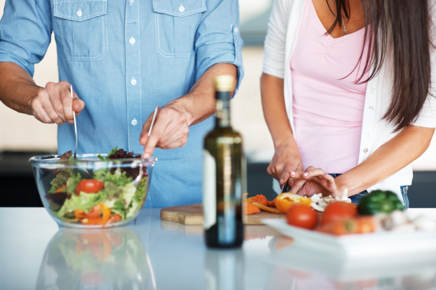 A man and woman preparing a salad in the kitchen.