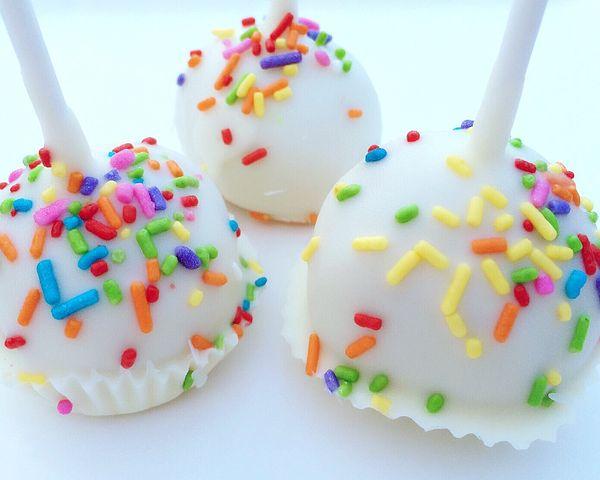 Three white cake pops with sprinkles on them.
