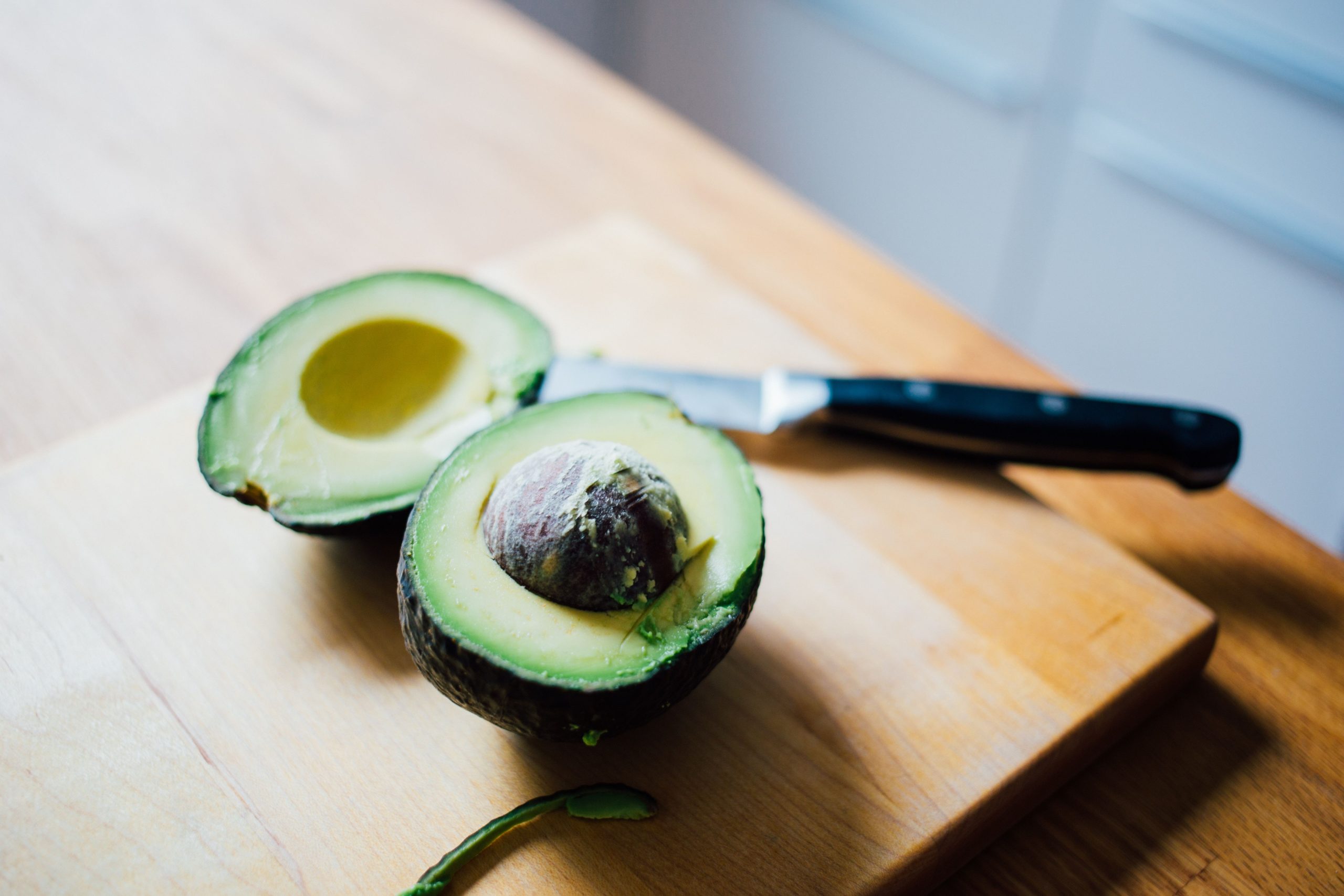 Two avocados on a cutting board with a knife.