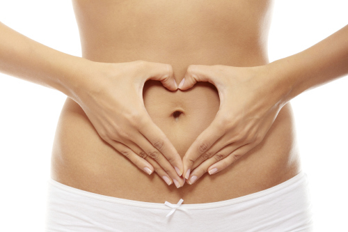 A woman's stomach with her hands making a heart shape.